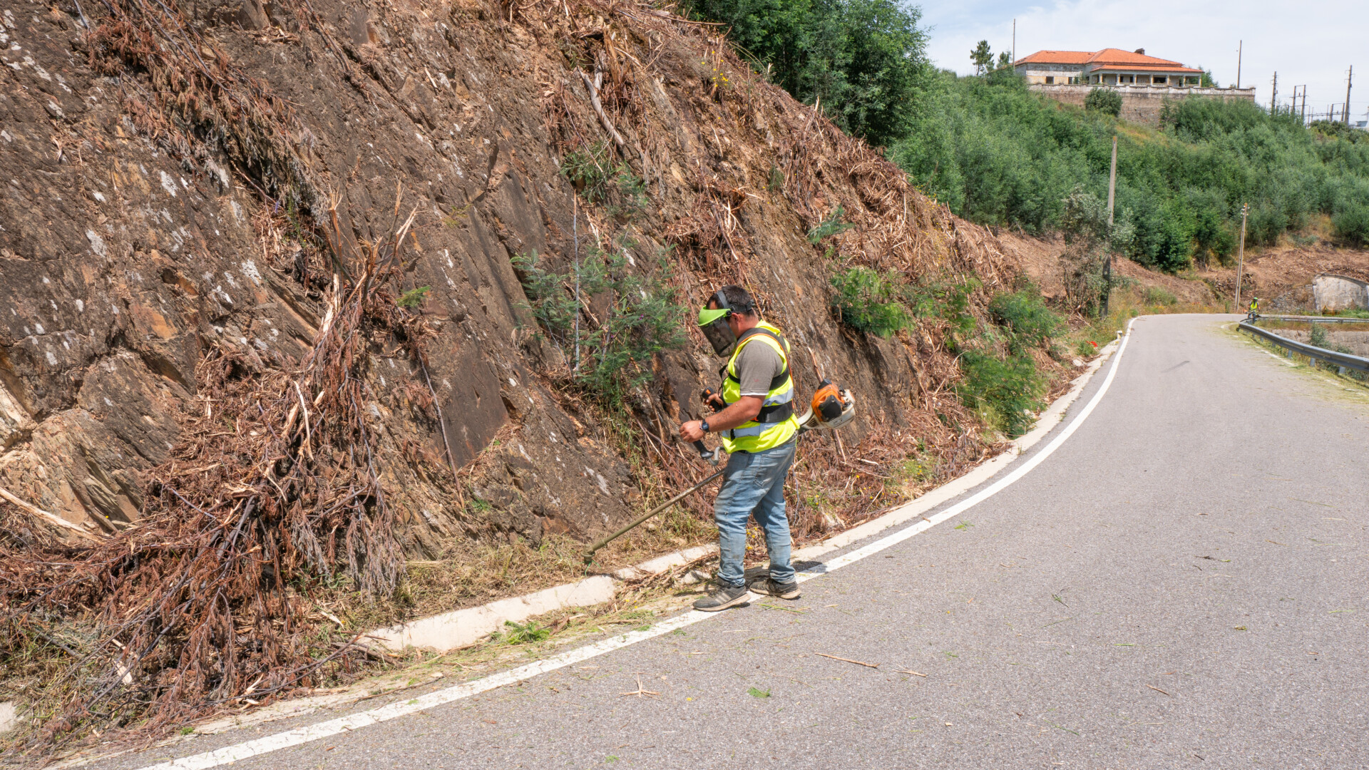 Limpeza de berma de estrada com roçadora, encosta já desmatada